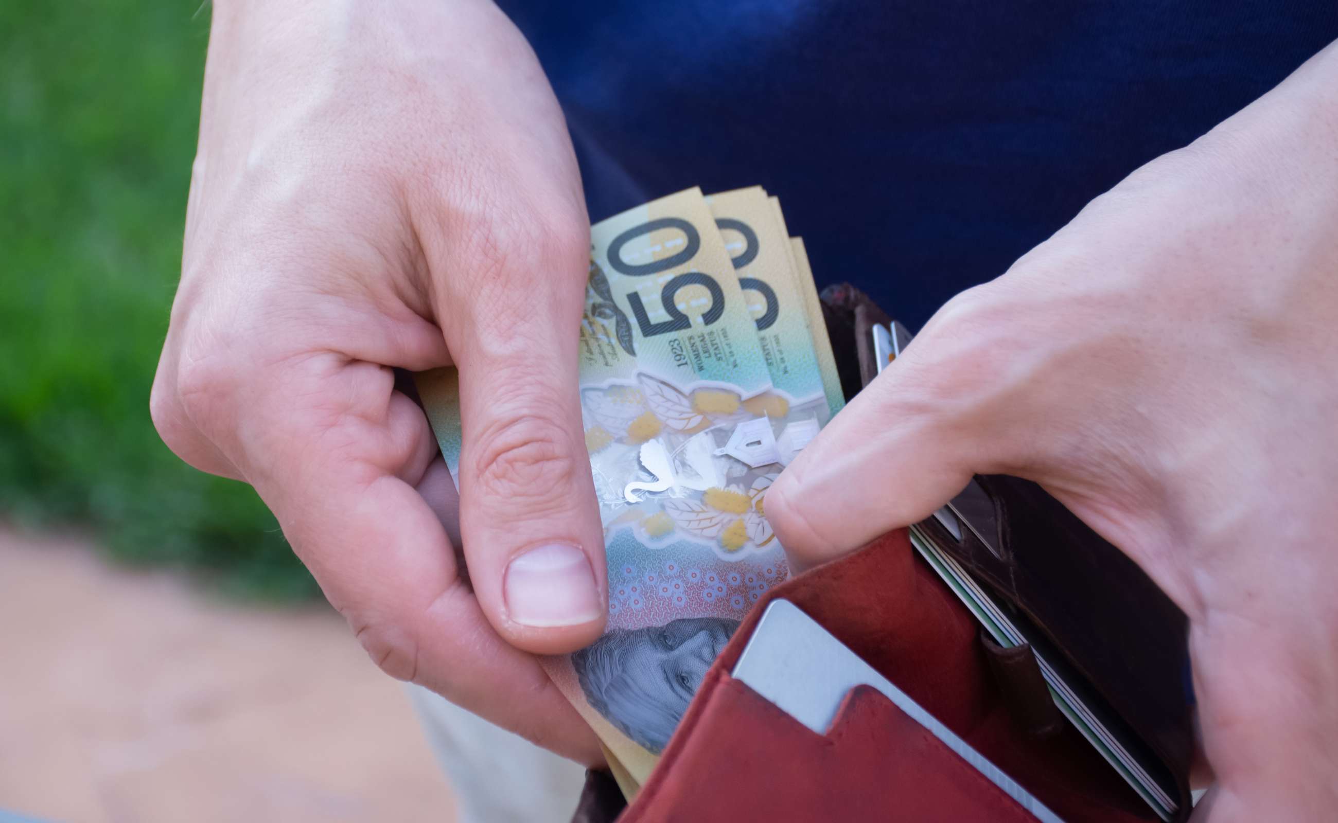 Image of a Person Pulling out $50 Notes from their Wallet | Featured image for the How Does Inflation Affect Car Prices Blog from Fido Finance.