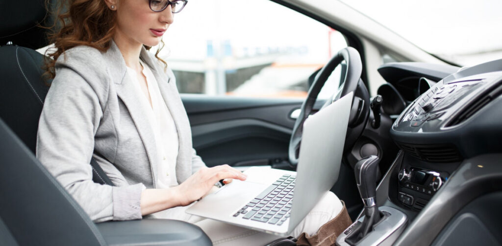 Businesswoman in a car with her computer | Featured image for the Self Employed Car Finance – What You Need to Know blog by Fido Finance.